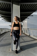 © Westend61 - Sporty woman with headphones standing on bridge, listening music, using smartphone