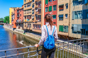 Wall Mural - Tourist woman see on colorful red and yellow houses and bridge river Onyar in Girona, Catalonia, Spain. Scenic ancient town. Famous tourist resort destination perfect place for holiday and vacation