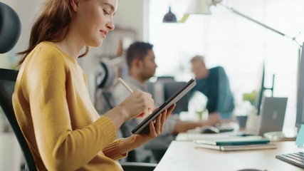 Aufkleber - Talented Female Designer Sitting at Her Desk She's Drawing, Writing and Using Pen with Digital Tablet Computer. Focus on Hands with Pen. Bright Office where Diverse Team of Young Professionals Work