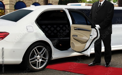 Photographie Chauffeur driver standing next to limo opened car door with red carpet