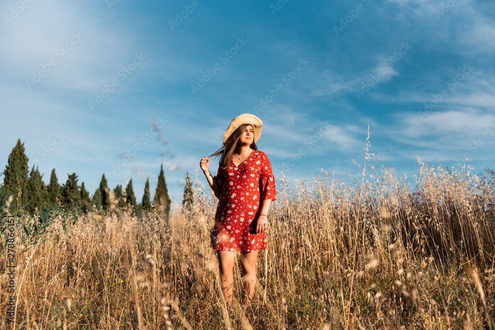 Attractive smiling woman in straw hat and red dress standing on wild ...
