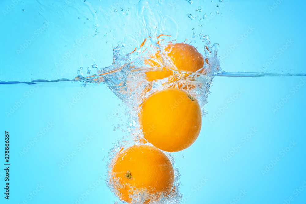 Falling of oranges into water on light background