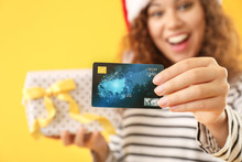 Happy African-American Woman In Santa Hat, With Gift And Credit Card On Color Background