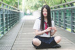 © atiger - Asian girl student in school uniform Japanese style, sit on a wooden bridge in sun shine, looking and smiling at camera with hands on her black long hair.