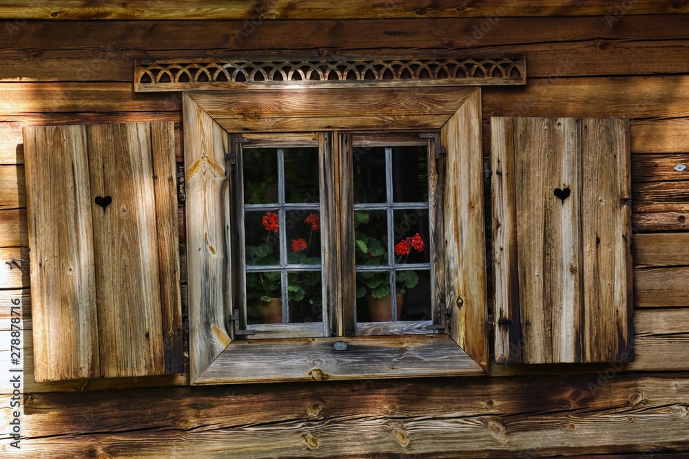 Drewniany dom z drewnianymi okiennicami, ozdobami i pelargoniami w oknach - obrazy, fototapety, plakaty 