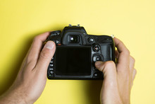 Digital Single Lens Reflex on yellow background, screen off view from above. Hand touching the camera