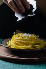 Female hands grating parmesan cheese, black truffle onto pasta tagliatelle.