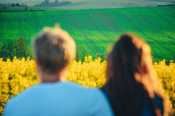 Couple in love looking at beautiful spring nature. Yellow and green agricultural field in background