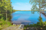 Fototapeta Na ścianę - Summer cozy landscape - a lake surrounded by trees, against the bright blue sky. The concept of peace, peace, unity with nature, Zen. Place for text.