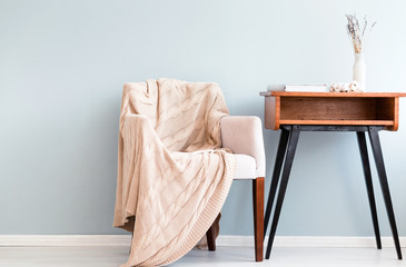 Armchair with plaid and retro table stand against a blue wall