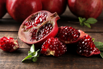 Wall Mural - Ripe tasty red pomegranate fruit with leaves on a brown wooden table. close-up