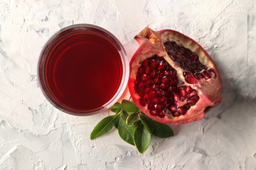 Wall Mural - Ripe tasty red pomegranate fruit and pomegranate pieces with leaves and juice on a light concrete background. top view