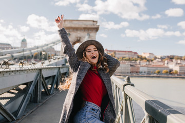 Wall Mural - blissful pale woman in coat expressing true emotions while posing on bridge in warm day. pleased whi