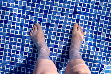 Feet of woman in the pool, dark blue water.