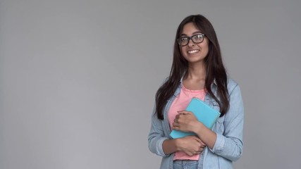 Wall Mural - Happy indian young woman college university student wear take off glasses hold book stand on grey studio background, smiling girl look at camera, education, laser vision correction concept, portrait