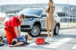 © rh2010 - Ambluence worker applying emergency care to the injured bleeding man lying on the pedestrian crossing, dispair woman driver standing on the background