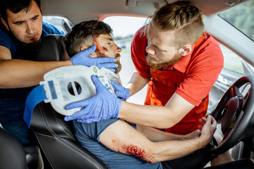 Wall Mural - Medics wearing neck corset to an injured man sitting in the car after the road accident, providing emergency medical assistance