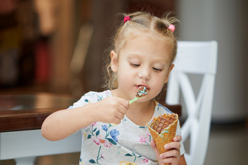 Happy baby girl eating licking big ice cream in waffles cone. happy laughing kid tasting dessert in cafe. It shows thumb up