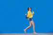 © Dusan Petkovic - Smiling Caucasian teenage girl in yellow blouse and with sunglasses holding orange juice while running in front of blue background.