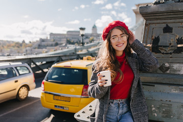 Wall Mural - omantic well-dressed girl in glasses posing with cup of coffee near road. amazing caucasian young la