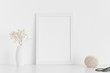 White frame mockup with workspace accessories  and gypshophila in a vase on a white table.Portrait orientation.