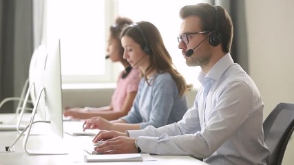Wall Mural - focused male call center agent in wireless headset helping customer