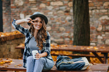 Lovable White Female Model With Curly Hairstyle Posing With Peace Sigh While Drinks Coffee In Park. Autumn Portrait Of Romantic European Woman In Checkered Shirt.