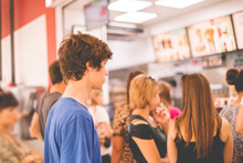 Young Teenager Standing In A Queue To Receive The Fastfood Package