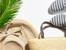 Summer Fashion Tropical Vacation Concept. Women's Female Beachwear Straw Hat Wicker Shoulder Bag Green Palm Leaves On White Stone Background. Creative Elegant Flat Lay