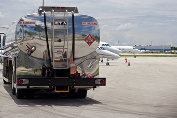 Tank truck on flight line with Jet A Fuel, no smoking, and hazmat placard on tank, air field with business jets blurred in background