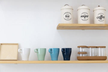 metal can of coffee or tea and glass cup on wooden shelf with white wall.