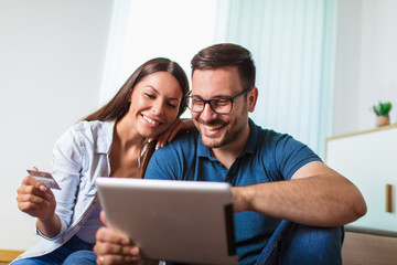 Smiling happy couple with tablet pc computer and credit or bank card shopping online at home