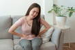 © sorrapongs - asian woman with menstruation and pain period cramps. young women having painful sitting on sofa at her home