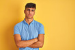 © Krakenimages.com - Young indian man wearing blue polo standing over isolated yellow background skeptic and nervous, disapproving expression on face with crossed arms. Negative person.