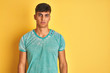 © Krakenimages.com - Young indian man wearing green t-shirt standing over isolated yellow background with serious expression on face. Simple and natural looking at the camera.