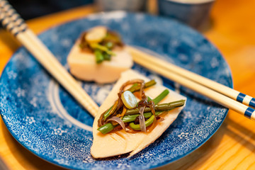 Traditional japanese blue ceramic plate in restaurant with wooden table and spring vegetable dish with takenoko shoots and sansai wild pickles