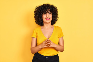 Sticker - Young arab woman with curly hair wearing t-shirt standing over isolated yellow background Hands together and fingers crossed smiling relaxed and cheerful. Success and optimistic