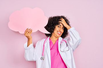 Sticker - Young arab woman with curly hair holding cloud speech bubble over isolated pink background stressed with hand on head, shocked with shame and surprise face, angry and frustrated. Fear and upset 