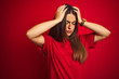 © Krakenimages.com - Young beautiful woman wearing t-shirt standing over isolated red background suffering from headache desperate and stressed because pain and migraine. Hands on head.