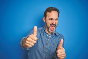 Handsome middle age senior man with grey hair over isolated blue background approving doing positive gesture with hand, thumbs up smiling and happy for success. Winner gesture.