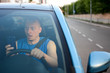 © Nenad - A man reads fake news over a smartphone while driving. Front view. Inside the car with smartphone.