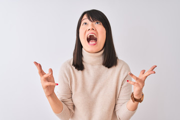 Wall Mural - Young beautiful chinese woman wearing turtleneck sweater over isolated white background crazy and mad shouting and yelling with aggressive expression and arms raised. Frustration concept.