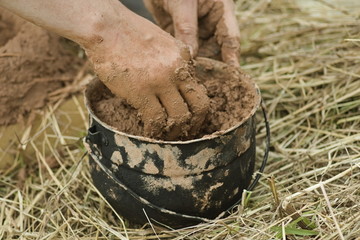 Hands of a potter kneading a clay in a camp bowler on a background of grass, in the summer outdoors