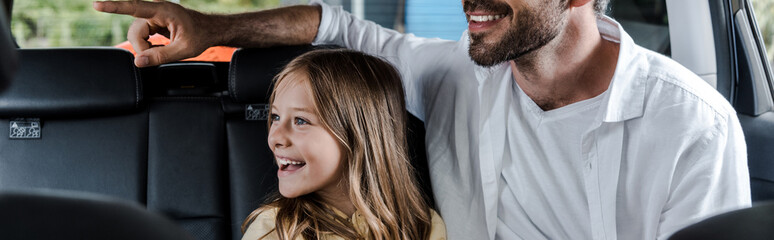 Wall Mural - panoramic shot of bearded pointing with finger near daughter in car