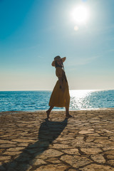 Wall Mural - young pretty smiling woman in yellow sundress walking by stone beach