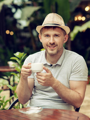 Wall Mural - Young successful positive man is sitting in a restaurant outdoors, drinking coffee and enjoying his weekend.