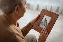Elderly Woman With Framed Family Portrait At Home