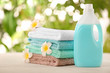 Pile of fresh towels, flowers and detergent on table against blurred background