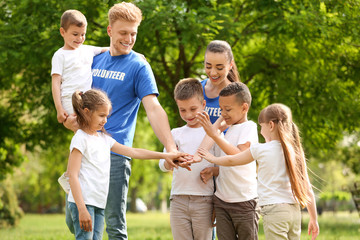 Wall Mural - Group of kids joining hands with volunteers in park