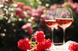 Glasses of rose wine on table in blooming garden, space for text